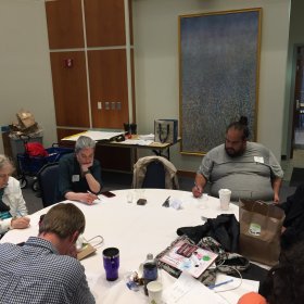 A group of 6 faculty is seated around a table, individually thinking about a mathematical task. 